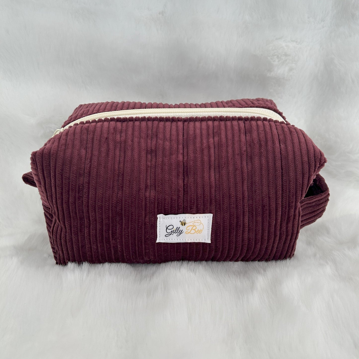 Maroon corduroy pouch with a visible brand label on a white background