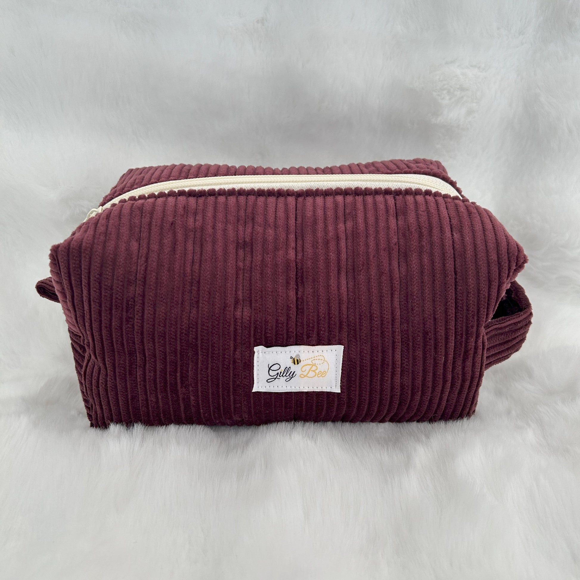 Maroon corduroy pouch with a visible brand label on a white background