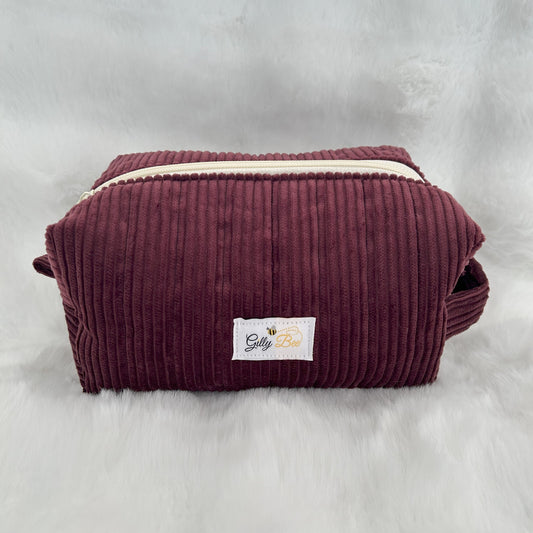 Maroon corduroy pouch with a visible brand label on a white background